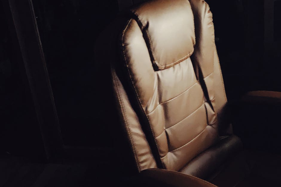 A brown leather office chair highlighted in dim lighting, showcasing luxury and comfort.