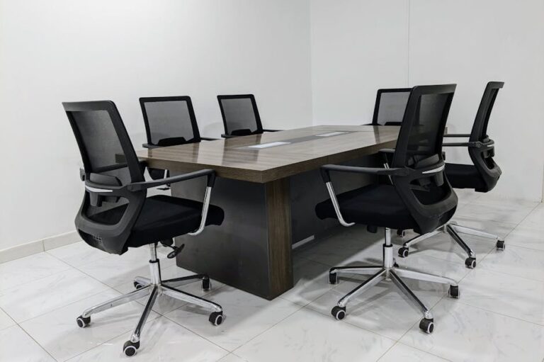 A neat and minimalistic conference room setup with black mesh chairs around a dark wooden table.