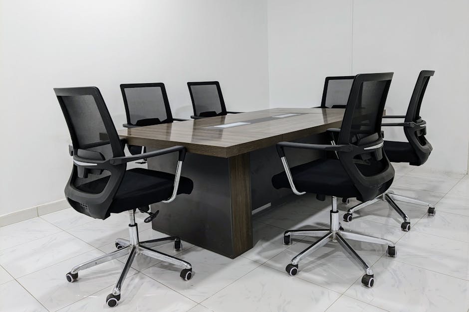 A neat and minimalistic conference room setup with black mesh chairs around a dark wooden table.