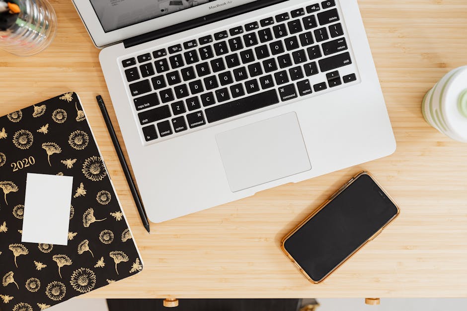 Flat lay of laptop, smartphone, and notebook on a wooden desk.