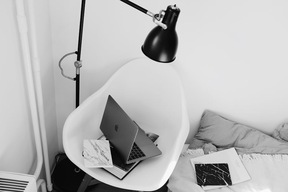 Stanowisko pracy w niewielkim mieszkaniu — laptop ustawiony przy ścianie pod lampą, w ciepłym świetle naturalnym.