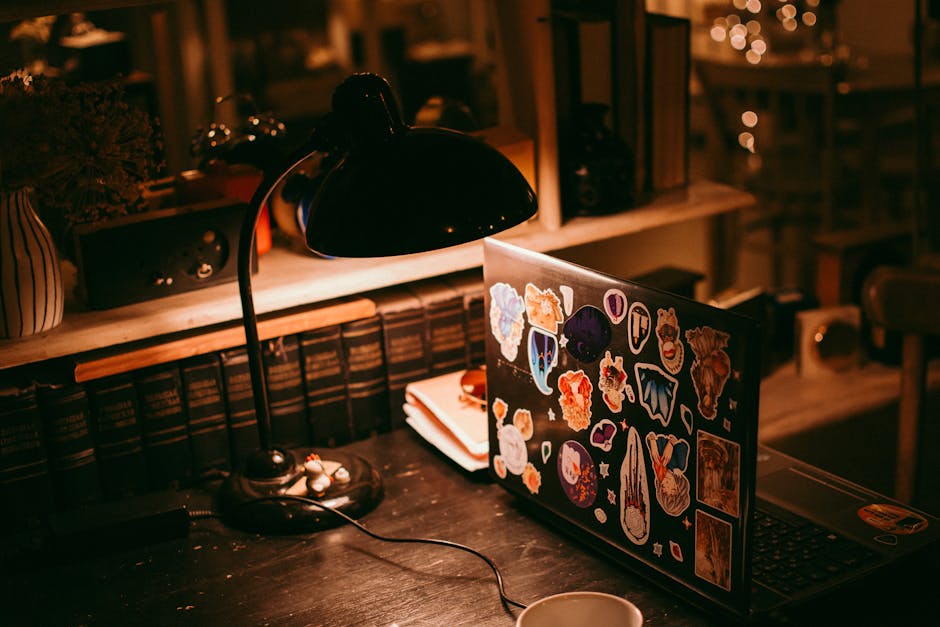 Warm lighting illuminates a workspace with a laptop, lamp, and books.